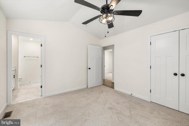 unfurnished bedroom with lofted ceiling, ensuite bath, light colored carpet, a closet, and ceiling fan