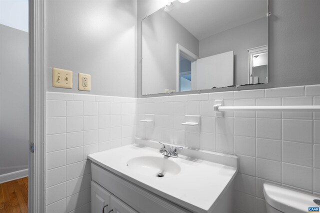 half bathroom with toilet, wood finished floors, tile walls, wainscoting, and vanity