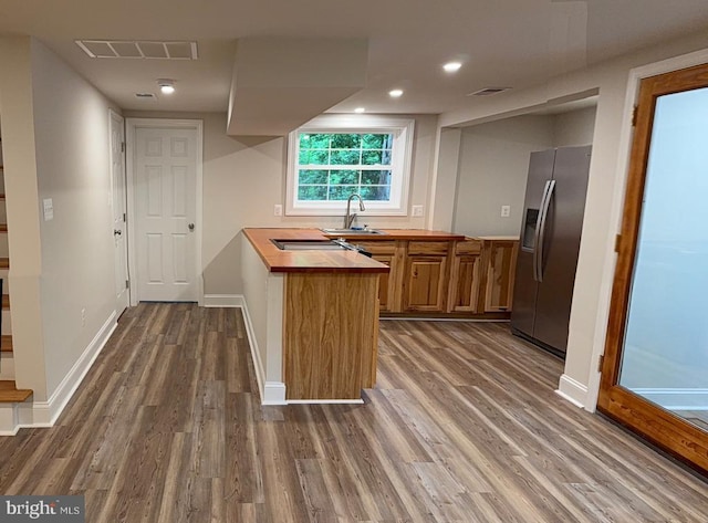  - kitchen featuring stainless steel refrigerator with ice dispenser, dark wood-style floors, brown cabinets, butcher block counters, and a peninsula