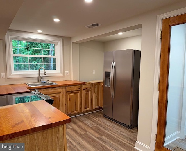  - kitchen featuring stainless steel fridge with ice dispenser, butcher block counters, light wood-style floors, recessed lighting, and brown cabinetry