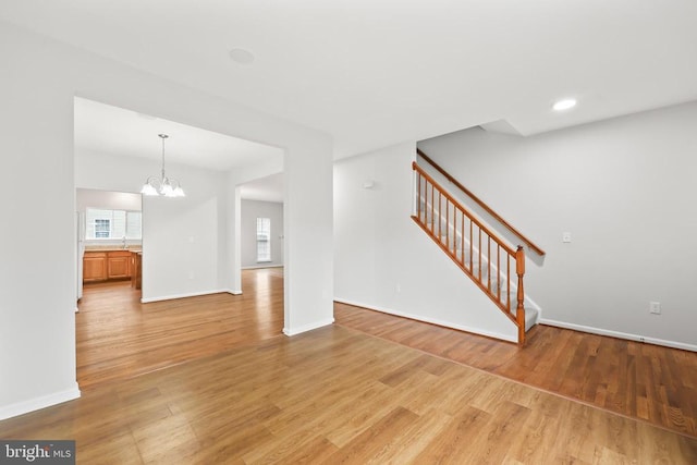 unfurnished living room featuring a chandelier, stairs, healthy amount of natural light, light wood-type flooring, and recessed lighting