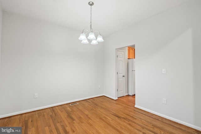 spare room with a chandelier, light wood finished floors, and baseboards