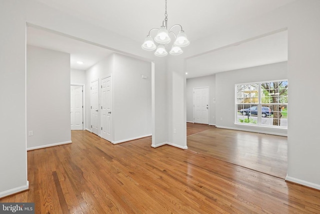unfurnished dining area featuring wood finished floors, a chandelier, and baseboards