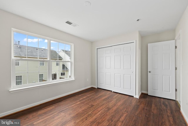 unfurnished bedroom with dark wood-style floors, baseboards, and a closet