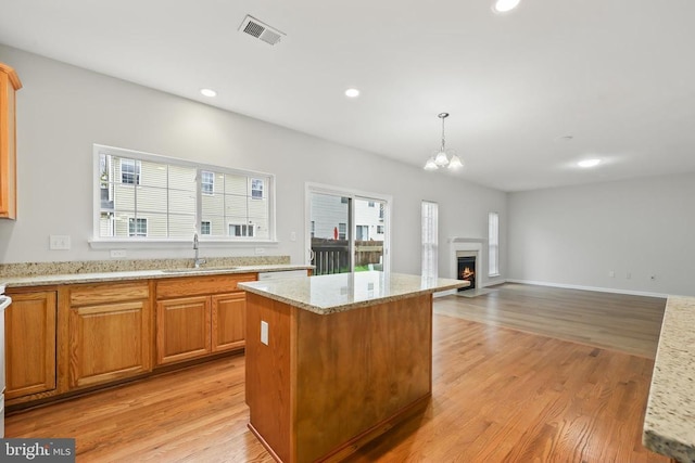 kitchen with a sink, light wood finished floors, a center island, light stone countertops, and recessed lighting