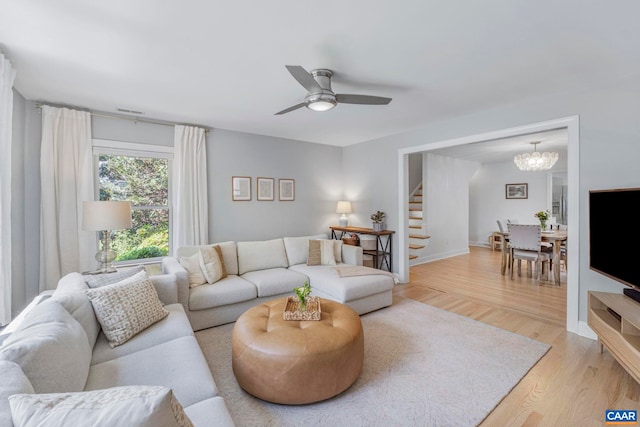 living room featuring light wood-type flooring, stairway, ceiling fan, and a chandelier