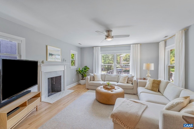 living room featuring wood finished floors, ceiling fan, a fireplace with flush hearth, and baseboards