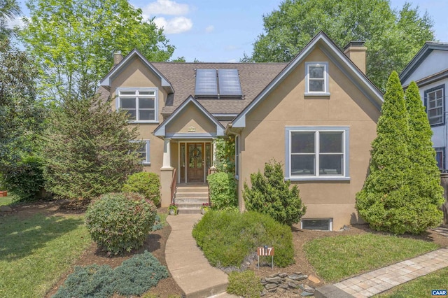 view of front of property featuring a chimney, stucco siding, roof mounted solar panels, a shingled roof, and a front yard