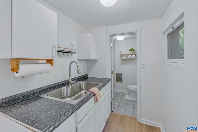 kitchen with a sink, white cabinets, light wood-style floors, and baseboards