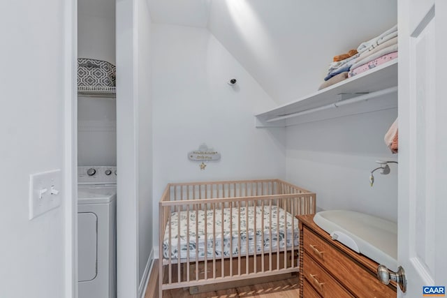 bedroom with washer / clothes dryer, a crib, wood finished floors, and vaulted ceiling
