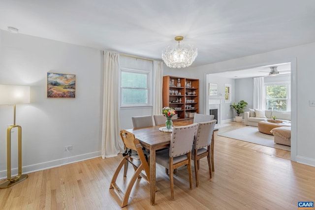dining room with a fireplace, light wood-style floors, a chandelier, and baseboards