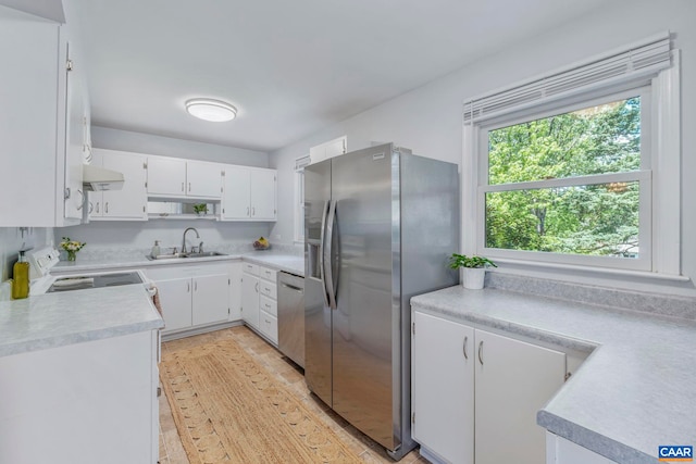 kitchen with stainless steel appliances, under cabinet range hood, a sink, light countertops, and white cabinets