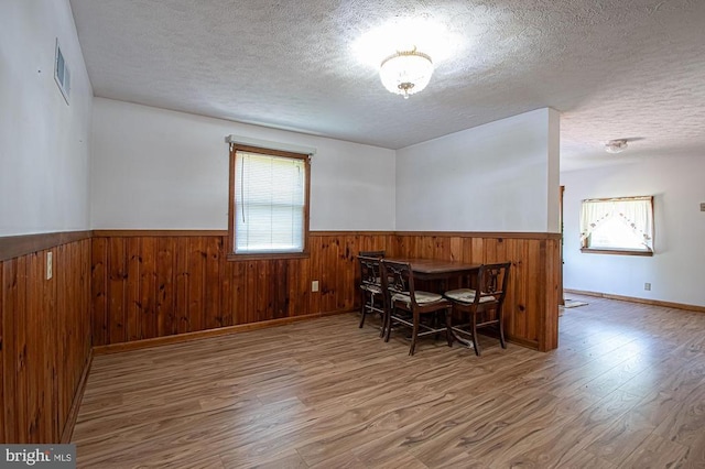 - dining space with a textured ceiling, a wainscoted wall, wood finished floors, and wooden walls