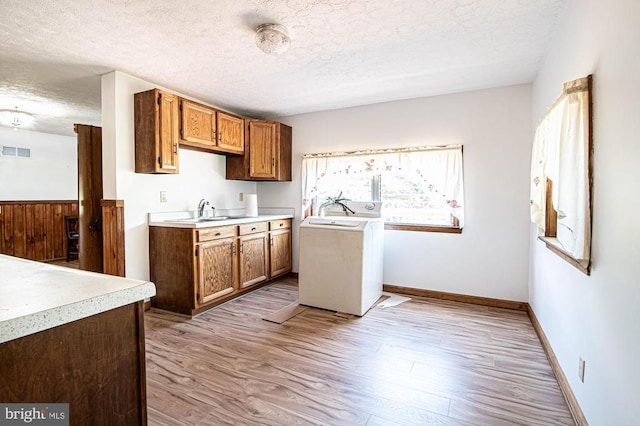  - kitchen featuring a textured ceiling, light countertops, light wood-style floors, washer / dryer, and brown cabinets