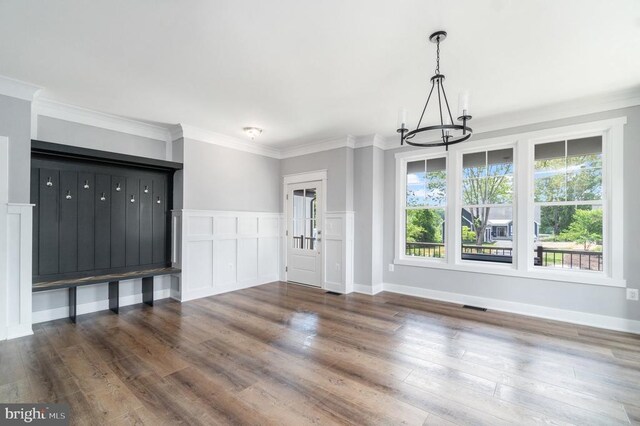 unfurnished living room featuring a chandelier, healthy amount of natural light, wood finished floors, and crown molding