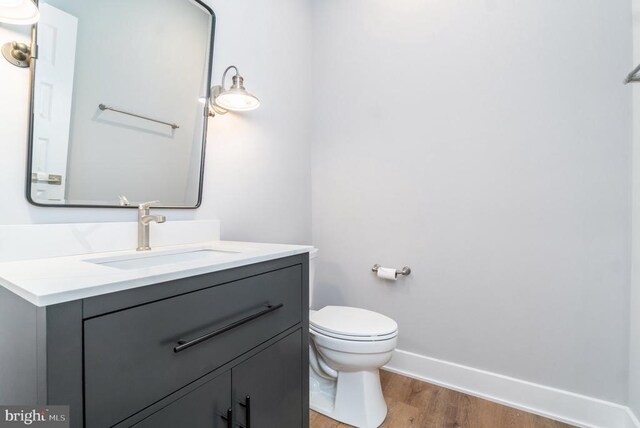 bathroom with baseboards, wood finished floors, toilet, and vanity