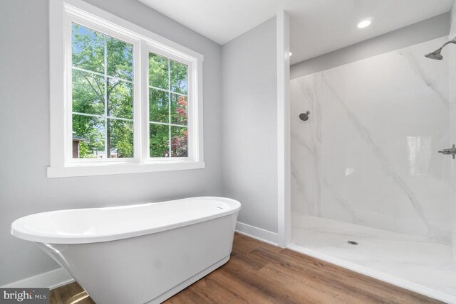bathroom with a marble finish shower, wood finished floors, baseboards, and a freestanding tub