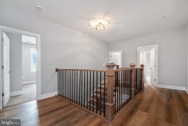 hallway with an upstairs landing, wood finished floors, and baseboards