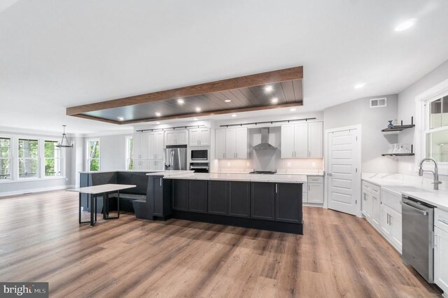 kitchen with stainless steel appliances, a sink, wall chimney exhaust hood, white cabinets, and light wood-style flooring
