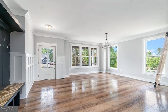 unfurnished living room with a chandelier, healthy amount of natural light, wood finished floors, and ornamental molding