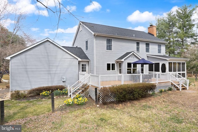 back of property with a sunroom, a chimney, a deck, a lawn, and roof with shingles