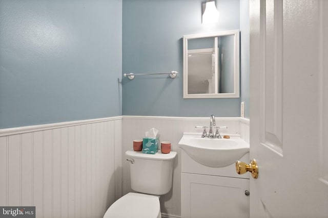 half bath with vanity, toilet, and wainscoting