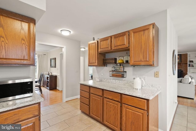 kitchen featuring stainless steel microwave, light tile patterned floors, baseboards, light stone countertops, and brown cabinets