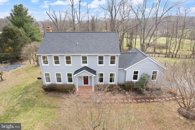 colonial home featuring a chimney, a front lawn, and a shingled roof