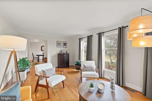 living area with baseboards, light wood-style floors, and ornamental molding