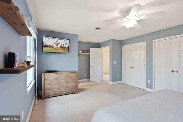 bedroom with two closets, baseboards, carpet flooring, and a ceiling fan