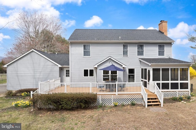 back of property with a sunroom, a chimney, a wooden deck, and a shingled roof