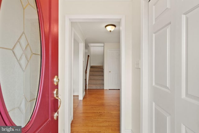 foyer featuring light wood finished floors, baseboards, stairway, and crown molding