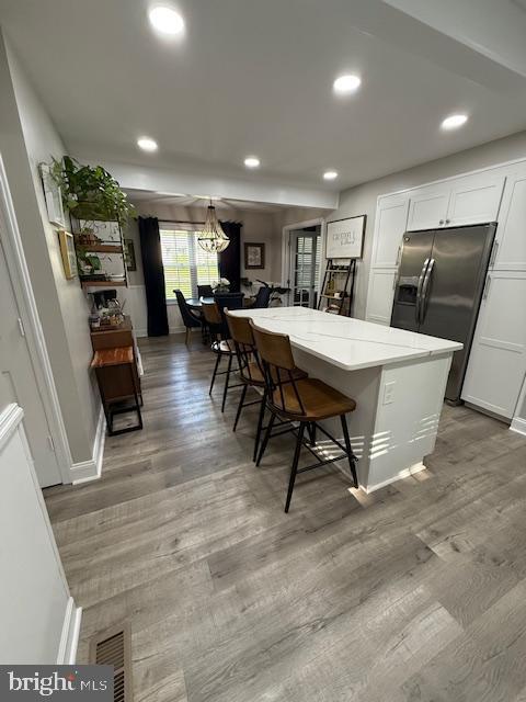 kitchen with stainless steel fridge with ice dispenser, white cabinetry, a chandelier, a breakfast bar area, and recessed lighting