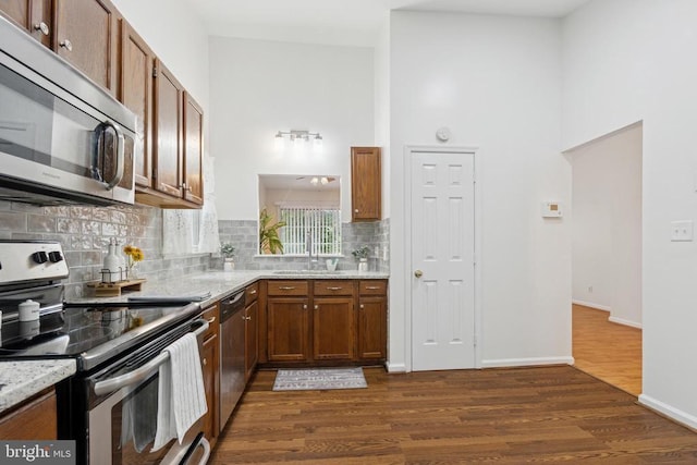 10804 Cobblestone Dr, Spotsylvania, VA 22553 - kitchen featuring stainless steel appliances, tasteful backsplash, dark wood-type flooring, light stone counters, and brown cabinetry
