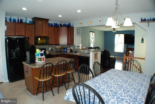  - kitchen featuring black appliances, a ceiling fan, backsplash, a breakfast bar, and pendant lighting
