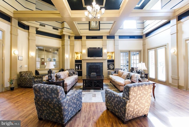 living area with a chandelier, a high ceiling, wood finished floors, a premium fireplace, and coffered ceiling