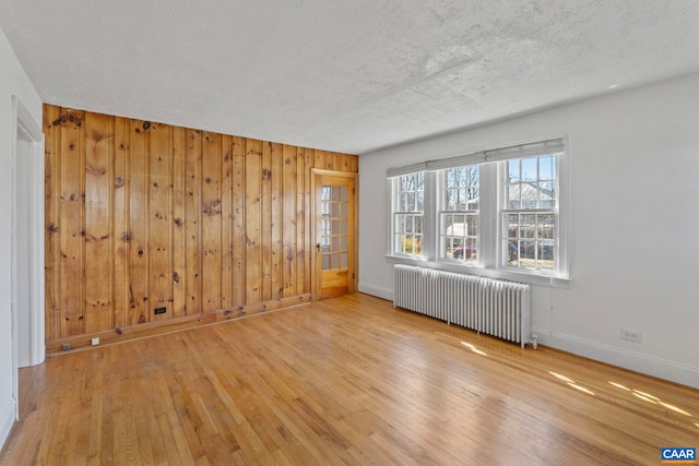 empty room with a textured ceiling, wood-type flooring, baseboards, and radiator heating unit