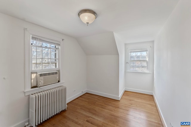 additional living space with radiator, cooling unit, a healthy amount of sunlight, and light wood-style flooring