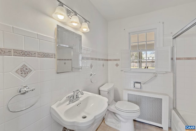 bathroom featuring a sink, tile walls, radiator, toilet, and shower / bath combination with glass door