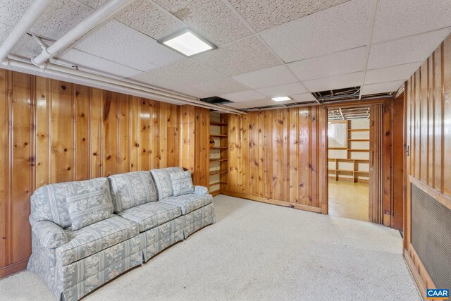 living area featuring a paneled ceiling, wooden walls, and carpet floors