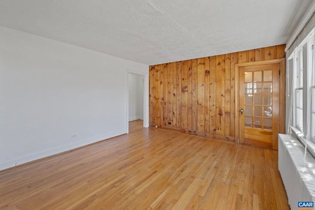empty room featuring baseboards, light wood finished floors, wooden walls, and radiator heating unit