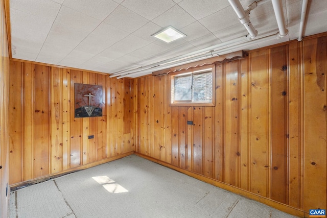 basement featuring carpet, wood walls, and baseboards
