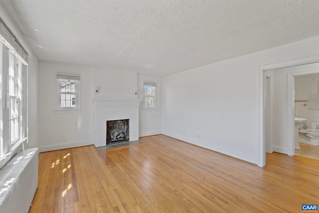 unfurnished living room featuring radiator, a fireplace, a textured ceiling, and a wealth of natural light