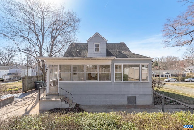 view of front facade with a sunroom, a shingled roof, and fence