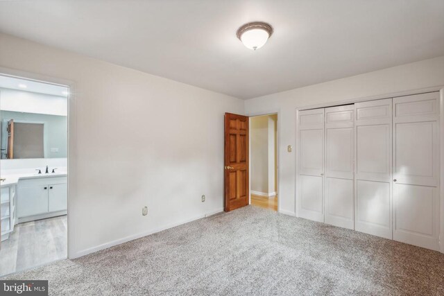 unfurnished bedroom featuring carpet, baseboards, a closet, and a sink