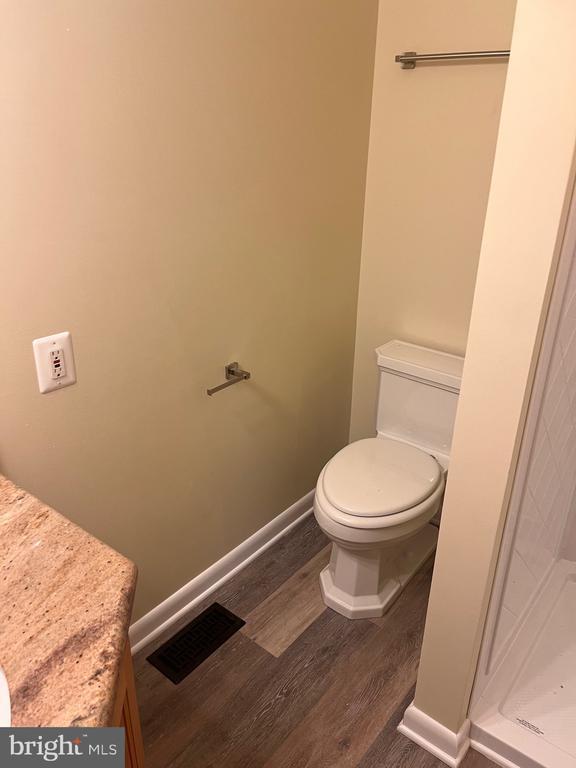 full bathroom featuring toilet, wood finished floors, a stall shower, and baseboards