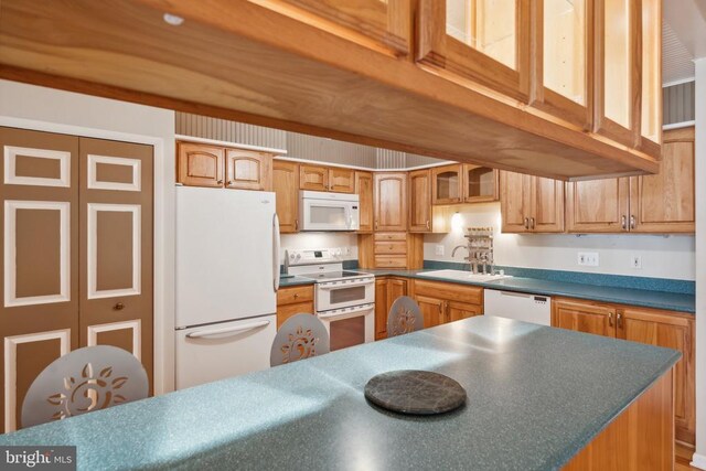 kitchen featuring white appliances, a sink, dark countertops, glass insert cabinets, and brown cabinets