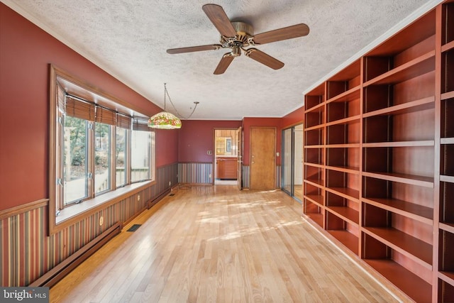 unfurnished living room with a textured ceiling, a wainscoted wall, wood finished floors, and a ceiling fan