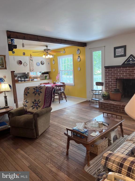  - living room featuring hardwood / wood-style flooring, a brick fireplace, ceiling fan, and beam ceiling