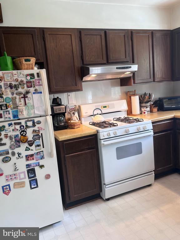  - kitchen with white appliances, under cabinet range hood, light countertops, and dark brown cabinets